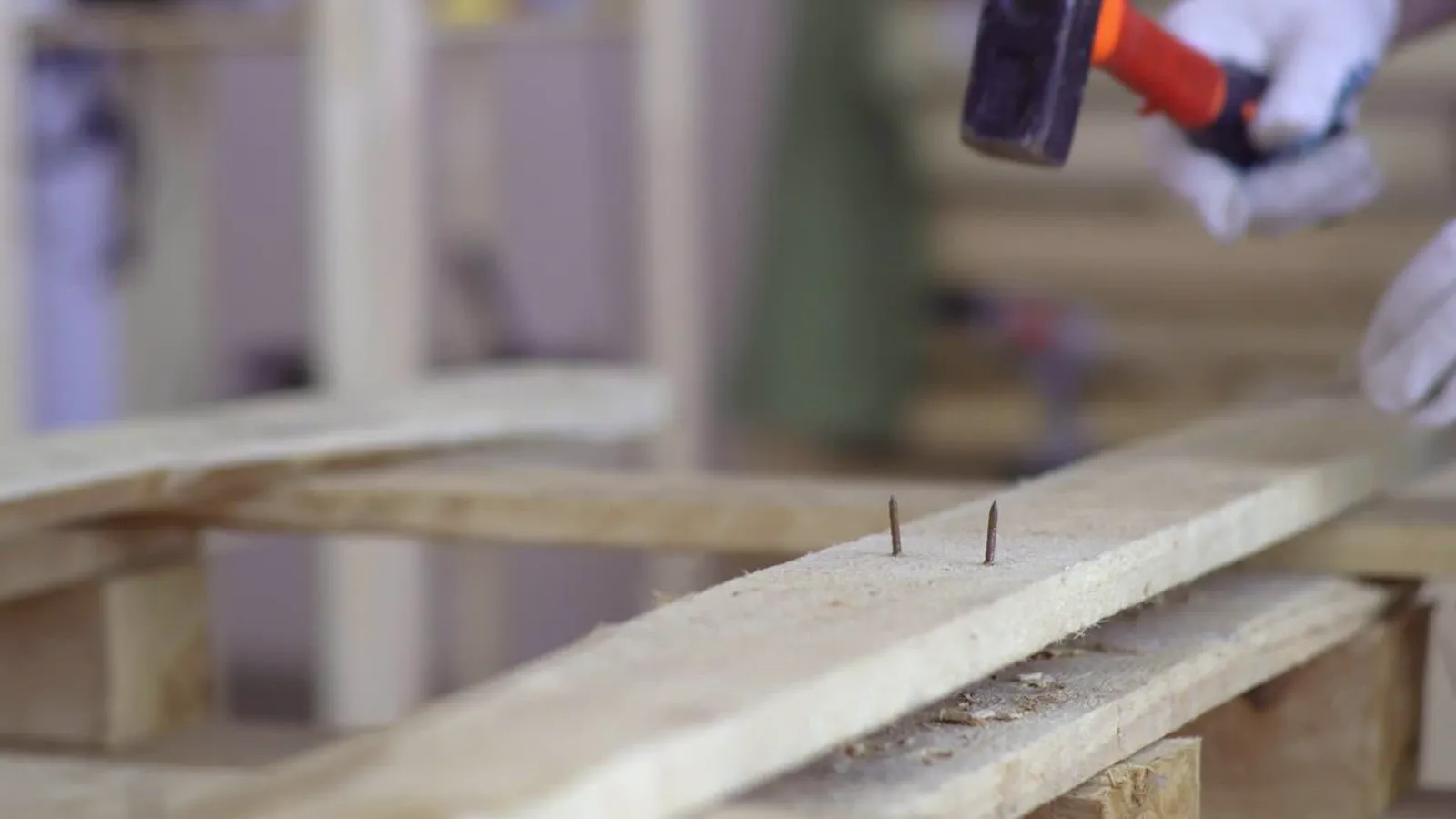 Gloved worker hammering a nail into a wooden board